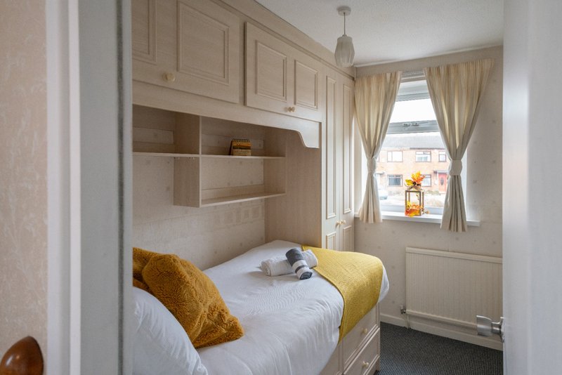 Compact bedroom with built-in bed, storage shelves, yellow cushions and window with curtains