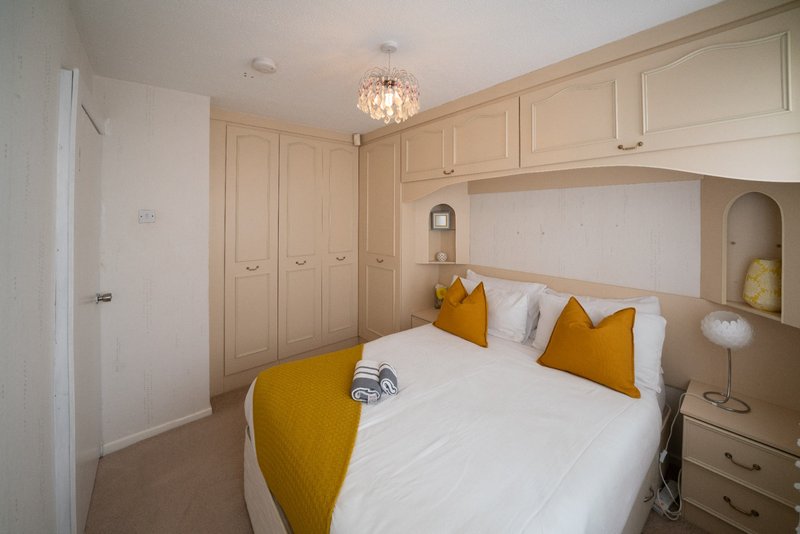 Modern bedroom with double bed, mustard cushions, fitted wardrobes and pendant ceiling light