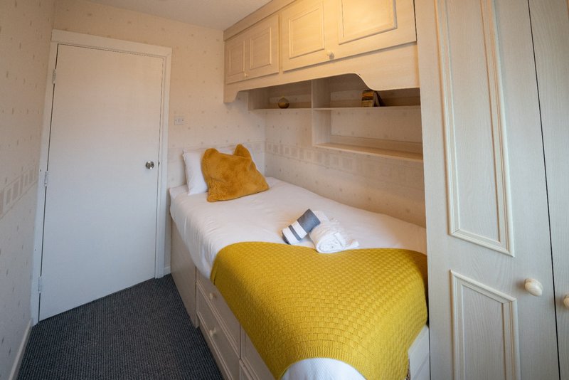 Compact bedroom with single bed, yellow bedding, mustard pillow, and built-in storage shelves