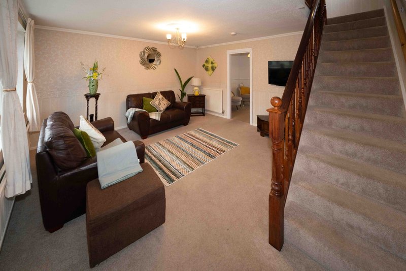 Spacious living room with brown leather furniture, striped rug, plants and staircase