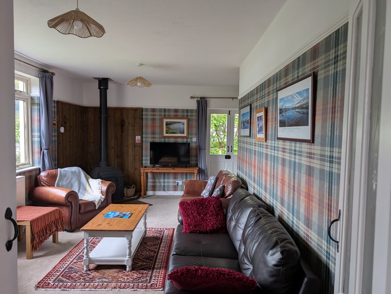 Spacious living room with fireplace, leather seating, plaid wallpaper and tartan furnishings