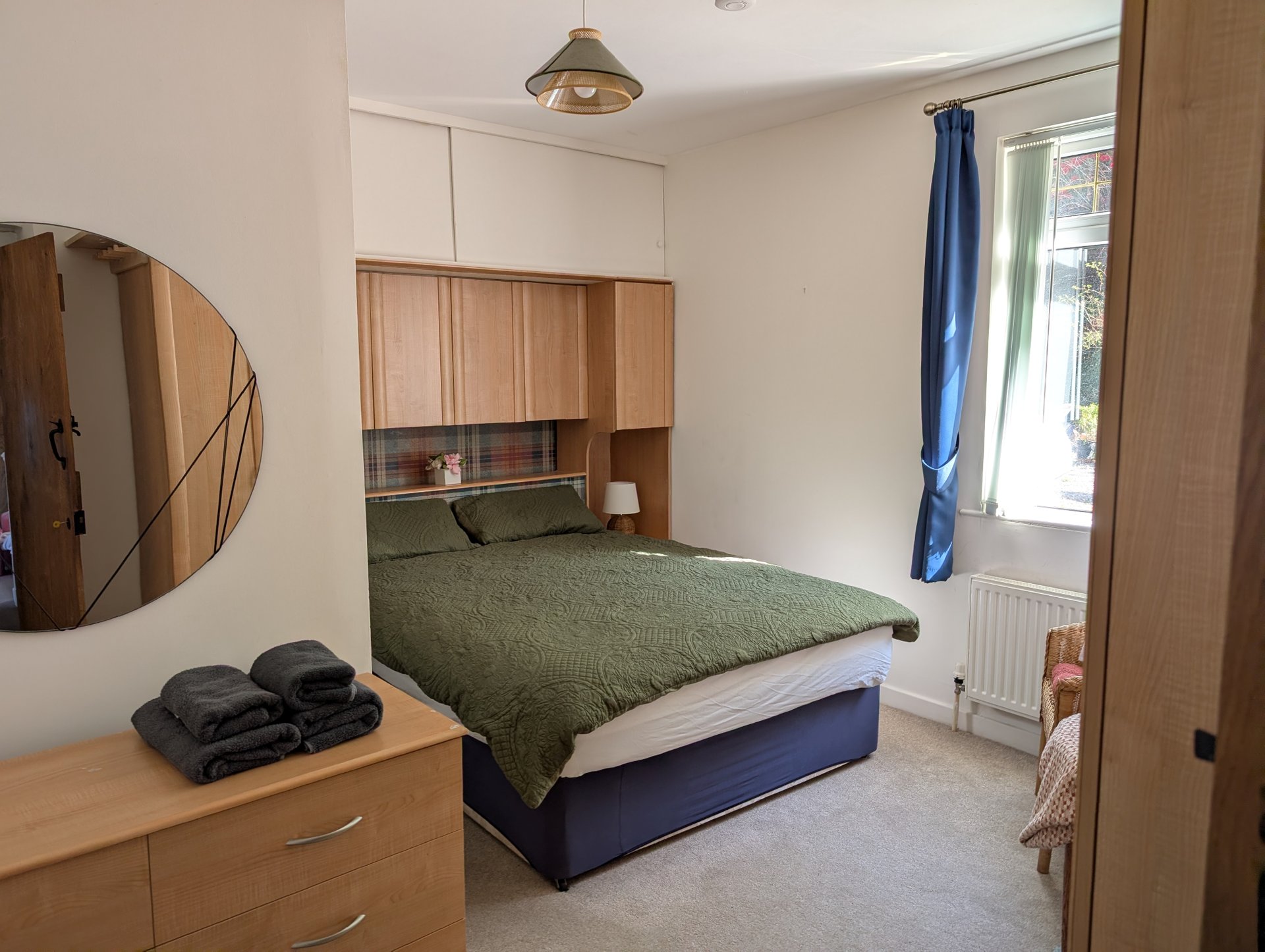 Bedroom with double bed, green bedding, wooden storage above headboard, mirror and dresser