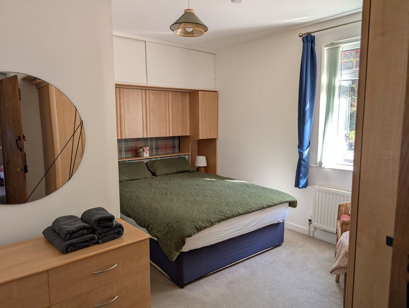 Bedroom with double bed, green bedding, wooden storage above headboard, mirror and dresser