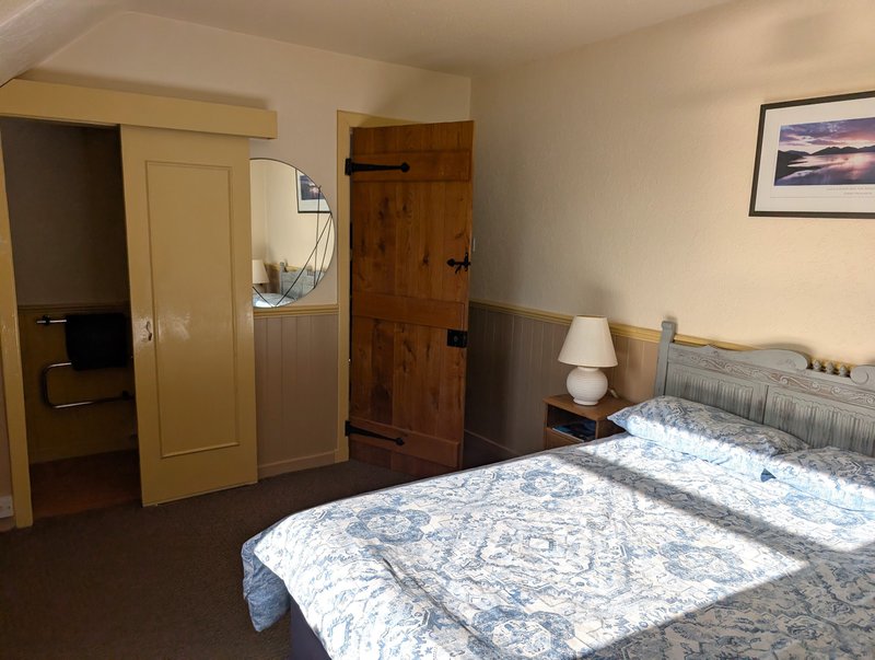Bedroom with double bed, bedside lamp, wooden doors, and framed landscape artwork
