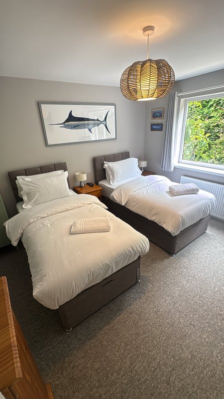 Bright bedroom with two single beds, woven pendant light, framed artwork and window with garden view