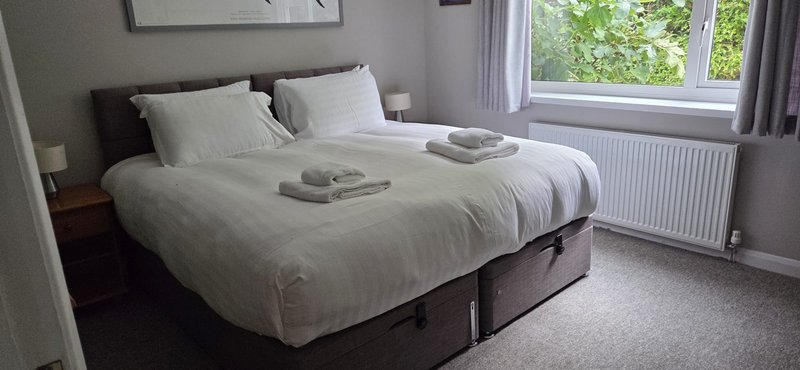 Bright bedroom with double bed, grey headboard, white bedding, radiator and large window