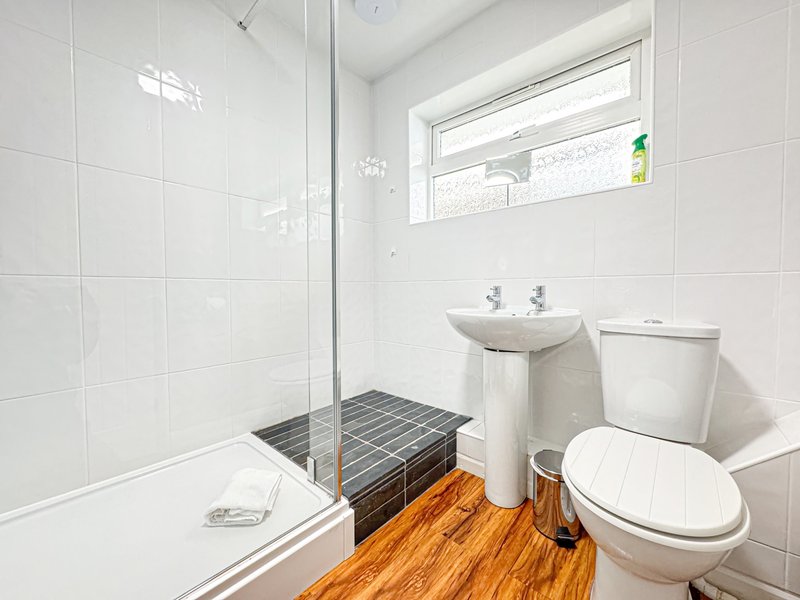 Modern bathroom with walk-in shower, pedestal sink, toilet and wooden floor