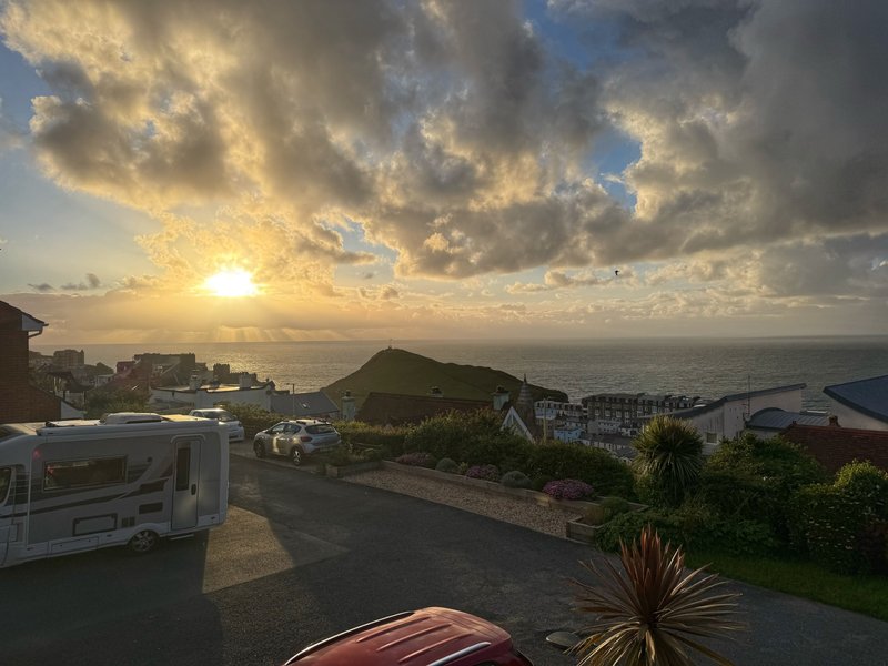Sunset view over coastal town with parked vehicles, palm trees and distant sea