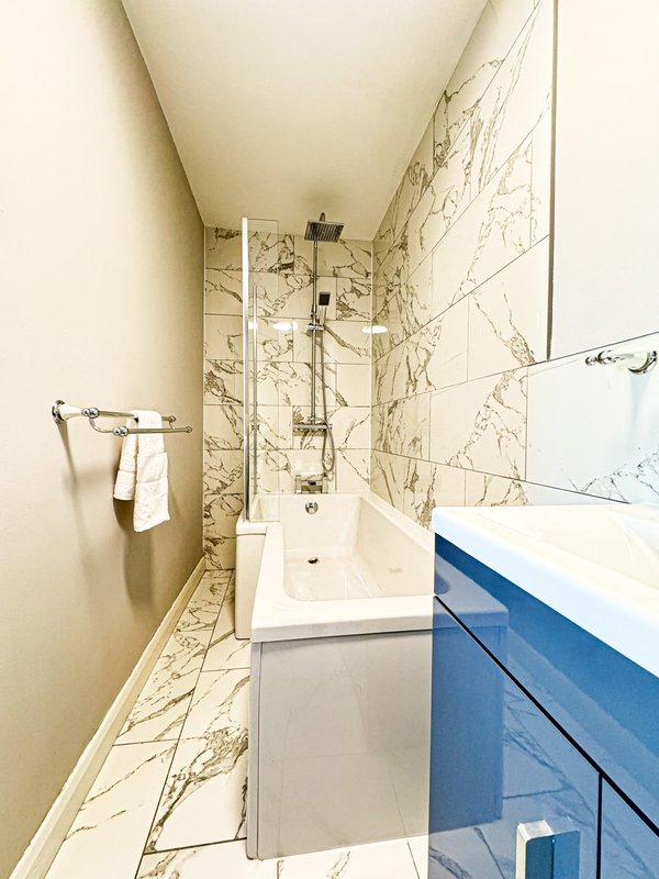 Modern bathroom with marble tiles, white sink, blue vanity, and glass shower enclosure
