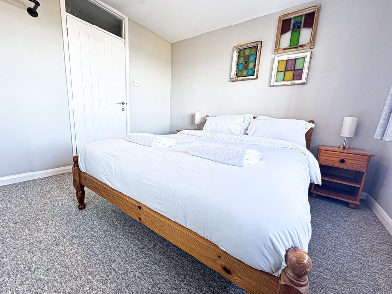 Bright bedroom with wooden bed, white bedding, wooden nightstand, and framed artwork on walls
