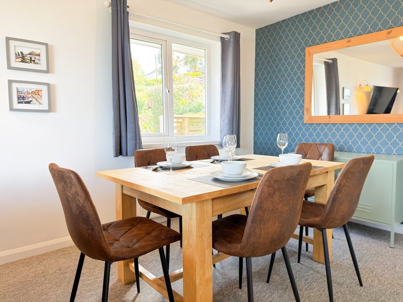 Dining room with wooden table, brown upholstered chairs, patterned blue wallpaper and large mirror