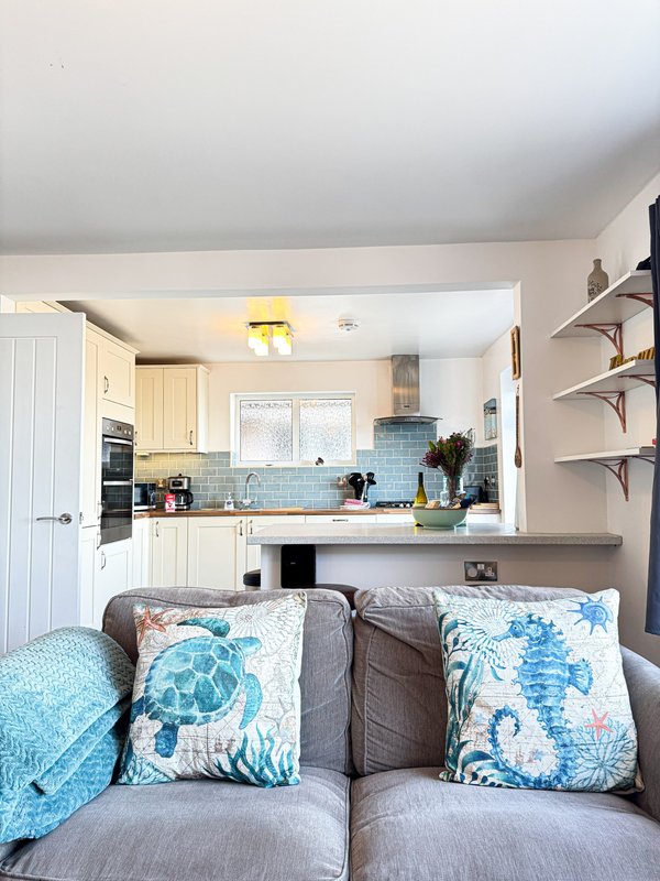 Open-plan living room with grey sofa and blue cushions, connected to modern kitchen with white cabinetry and blue tile backsplash