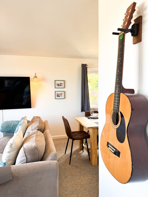 Bright living room with sofa, TV, desk, chair, and acoustic guitar on wall mount