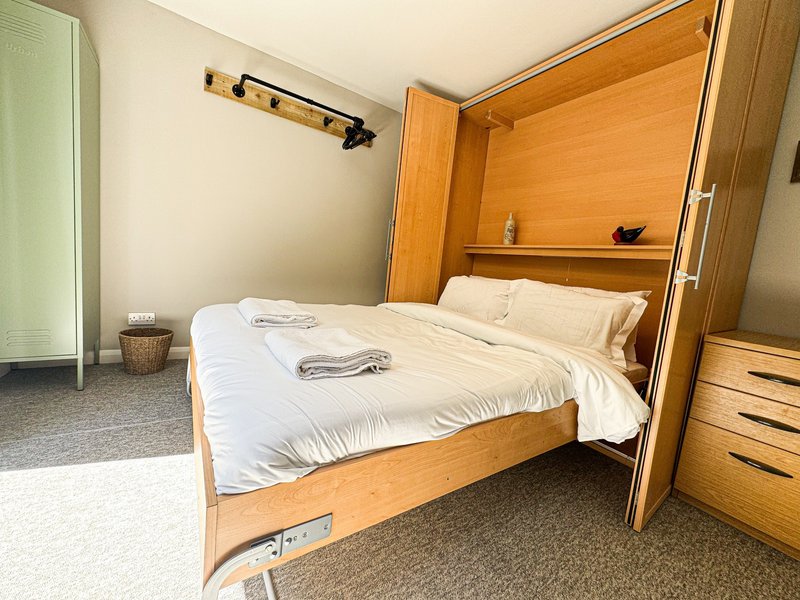 Bedroom with wooden bed frame, white bedding, storage headboard and carpeted floor