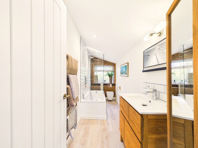 Modern bathroom with wooden vanity, white subway tile walls, mirror and bathtub