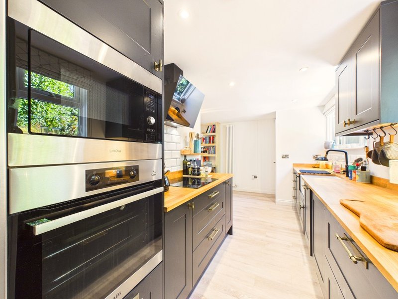Modern kitchen with black cabinetry, wooden countertops, built-in oven and bright natural light