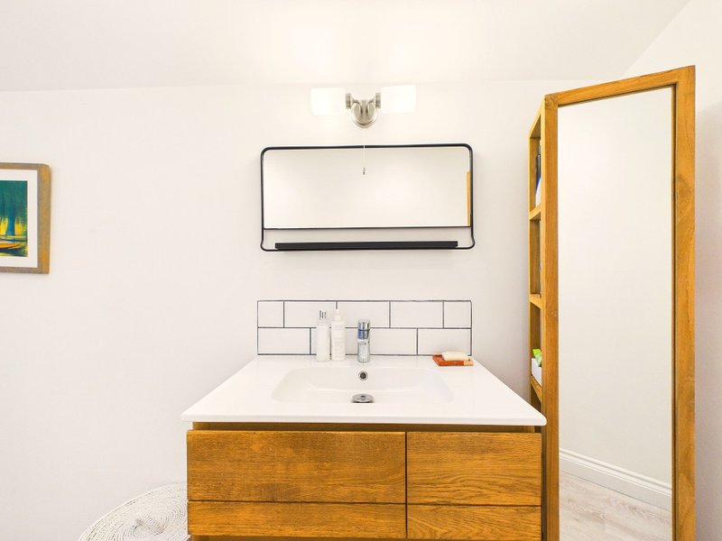 Bathroom with wooden vanity, white sink, mirror, and subway tile backsplash