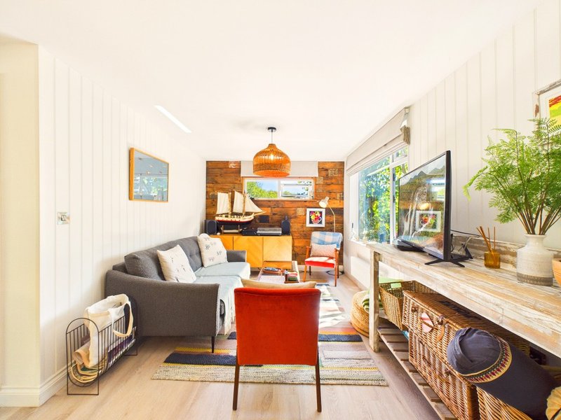 Open-plan living room with sofa, red chair, desk, kitchen area and natural light from windows