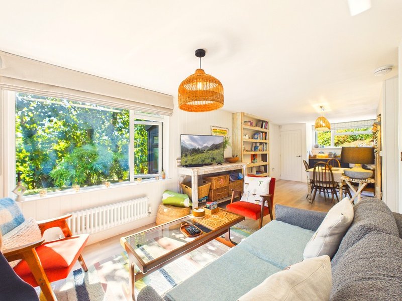 Bright open-plan living room with orange pendant lamp, grey sofa, wooden coffee table and garden views