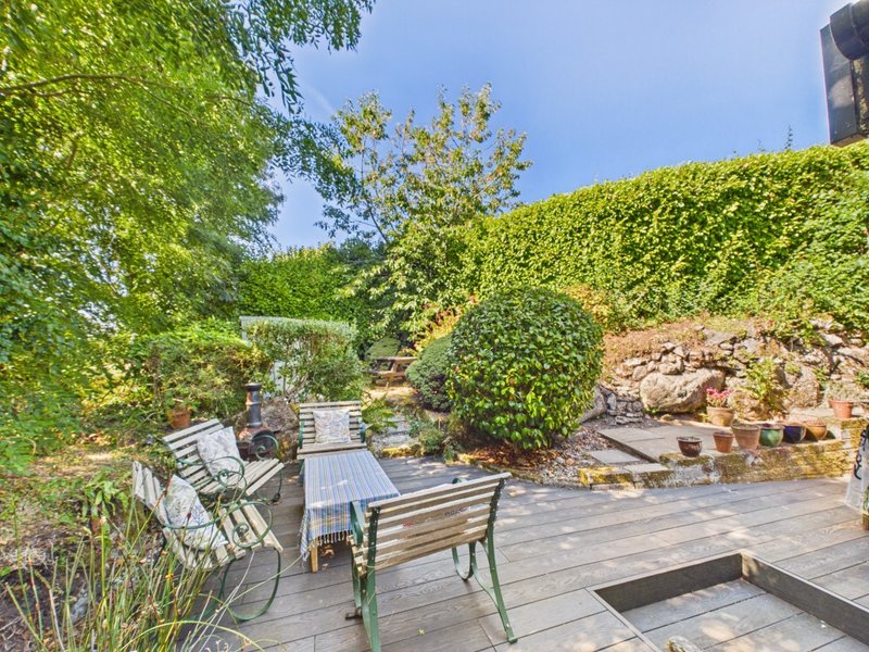 Garden patio with wooden benches, hedges, stone walls and clear blue sky