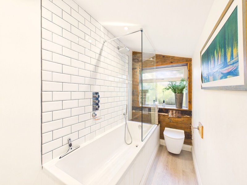 Modern bathroom with white subway tile, bathtub with glass screen, wooden vanity and framed artwork