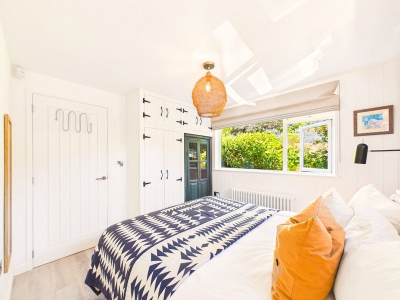 Bright bedroom with double bed, geometric patterned bedding, orange pendant light and garden views