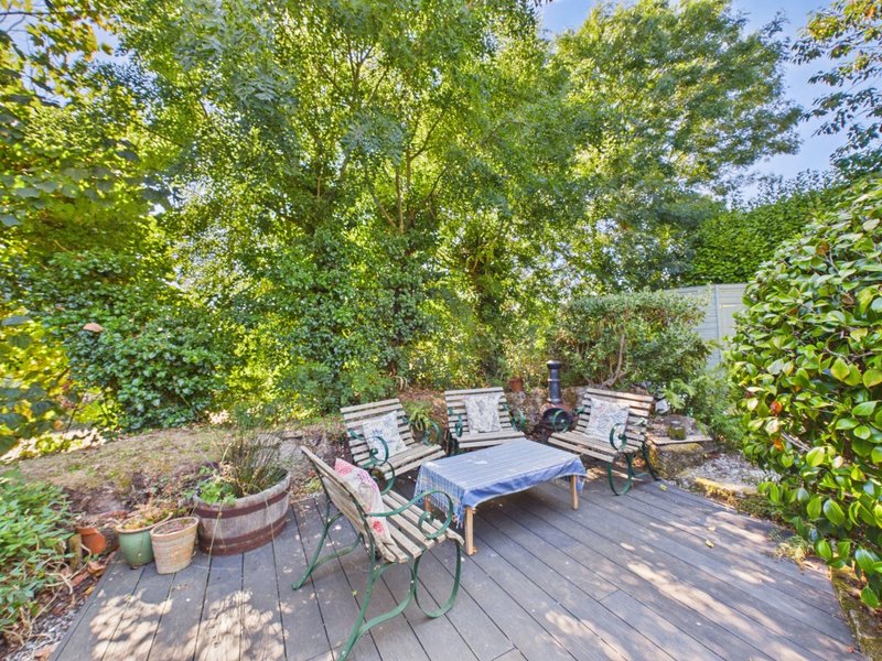 Shaded garden deck with seating area, potted plants, and mature trees overhead