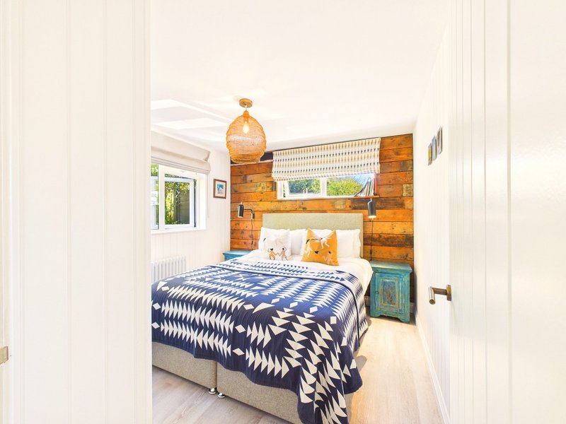 Bright bedroom with double bed, blue patterned bedding, wooden storage wall, and pendant lamp