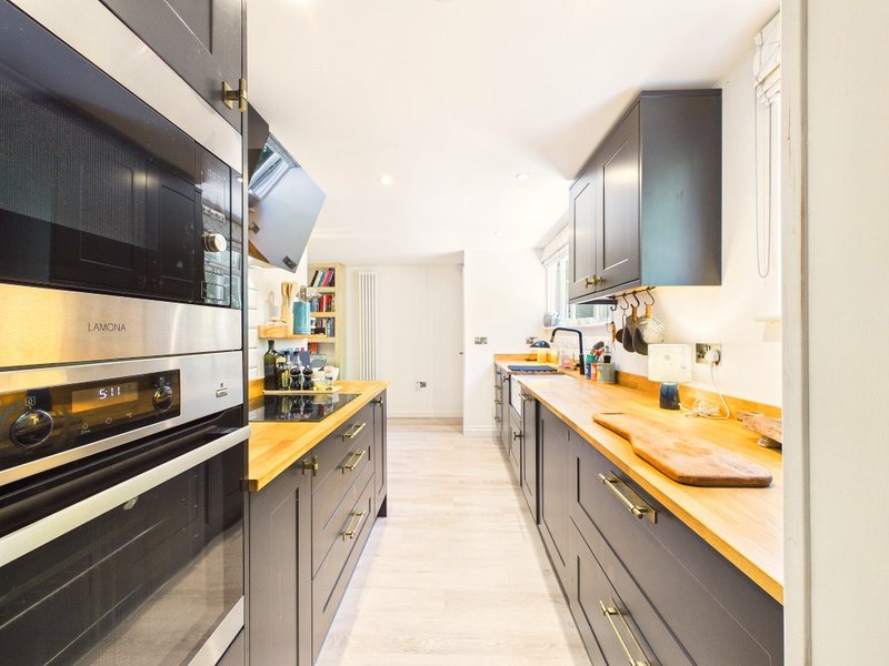 Modern galley kitchen with black cabinetry, golden countertops, stainless steel appliances