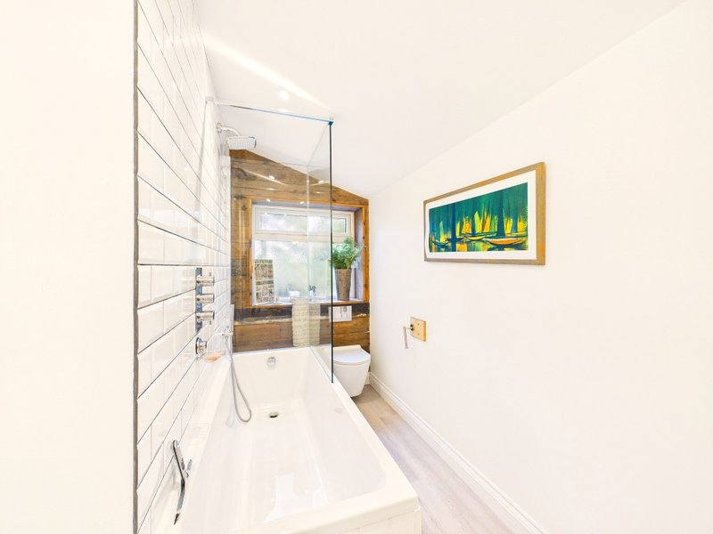 Modern bathroom with white subway tile walls, freestanding bathtub, glass shower enclosure, and framed artwork