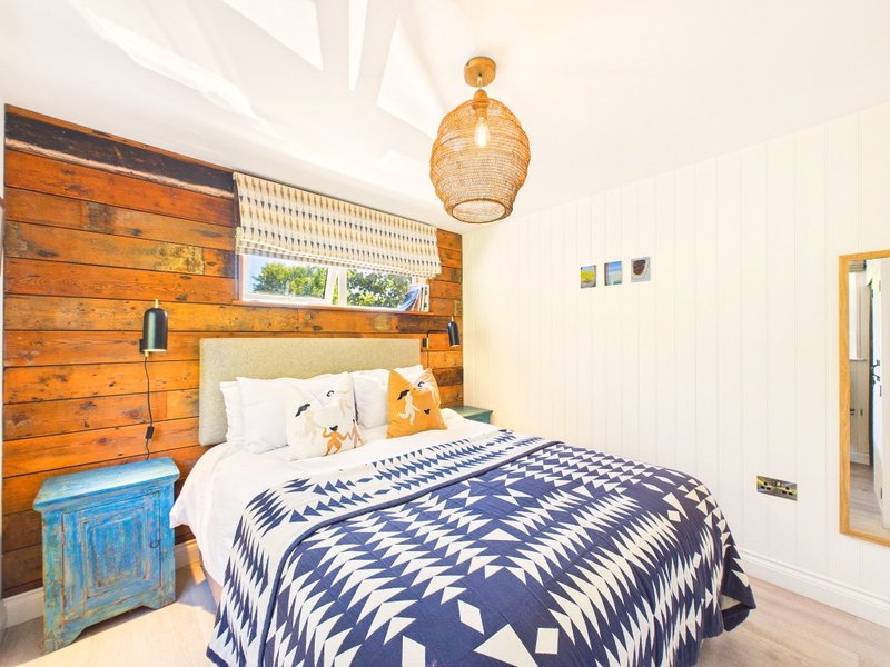 Bedroom with wooden feature wall, single bed, navy patterned bedding, and woven pendant lamp