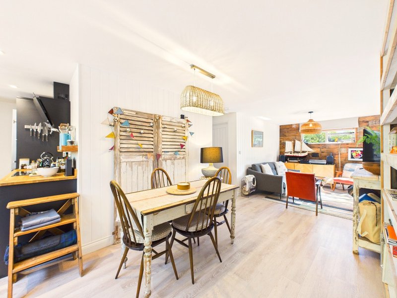 Open-plan living space with wooden dining table, chairs, kitchen area and shelving