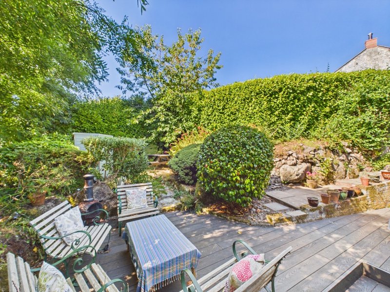 Garden patio area with seating, striped awning, hedges and stone walls