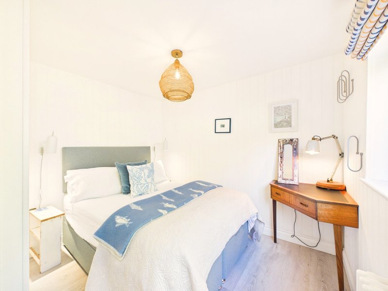 Bright bedroom with double bed, blue bedding, wooden desk, and amber pendant light