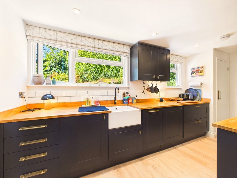 Modern kitchen with black cabinetry, orange countertops, white subway tile backsplash, and large windows