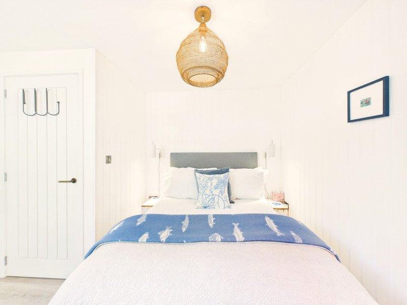 Bright bedroom with double bed, blue patterned duvet, woven pendant light, and white wardrobe