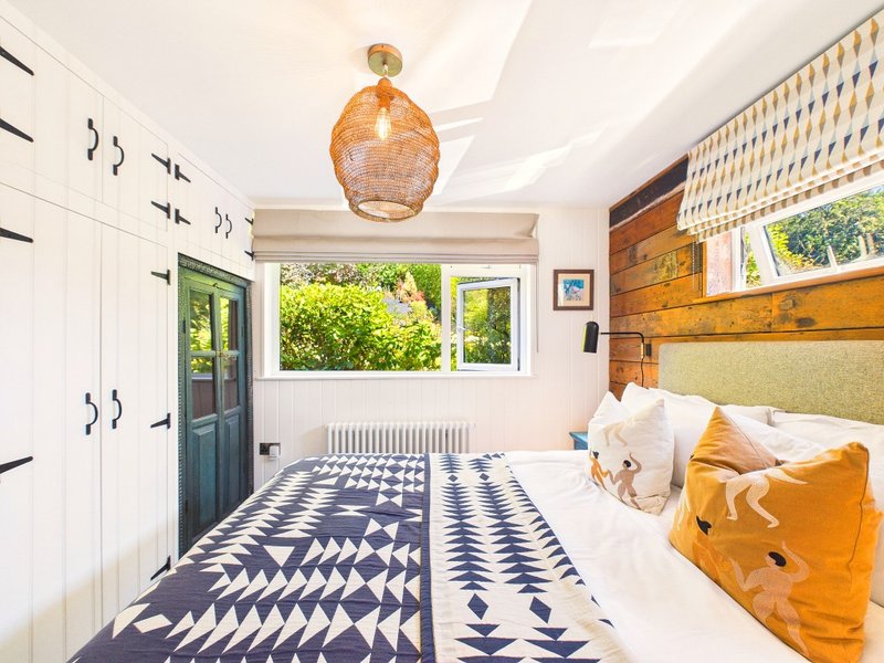 Bright bedroom with double bed, patterned blue and white rug, woven pendant light, and garden views