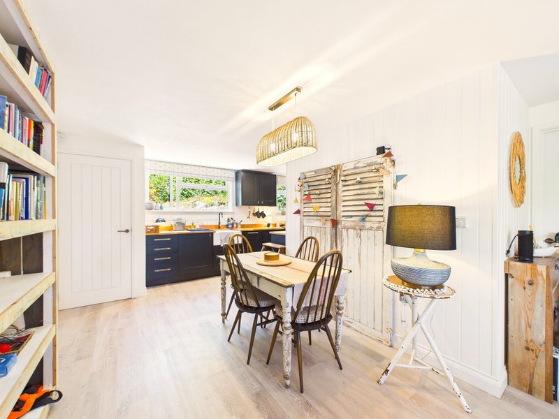 Open-plan kitchen and dining area with wooden table, chairs, shelving, and pendant lighting