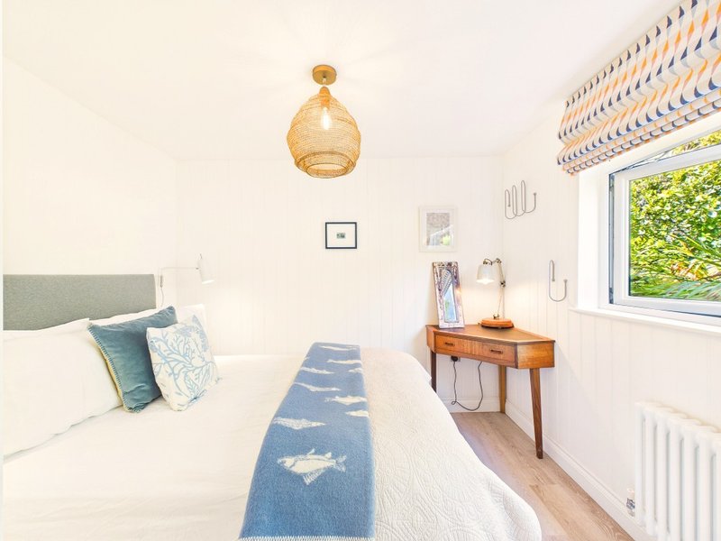 Bright bedroom with double bed, blue runner, wooden desk, pendant light and garden view