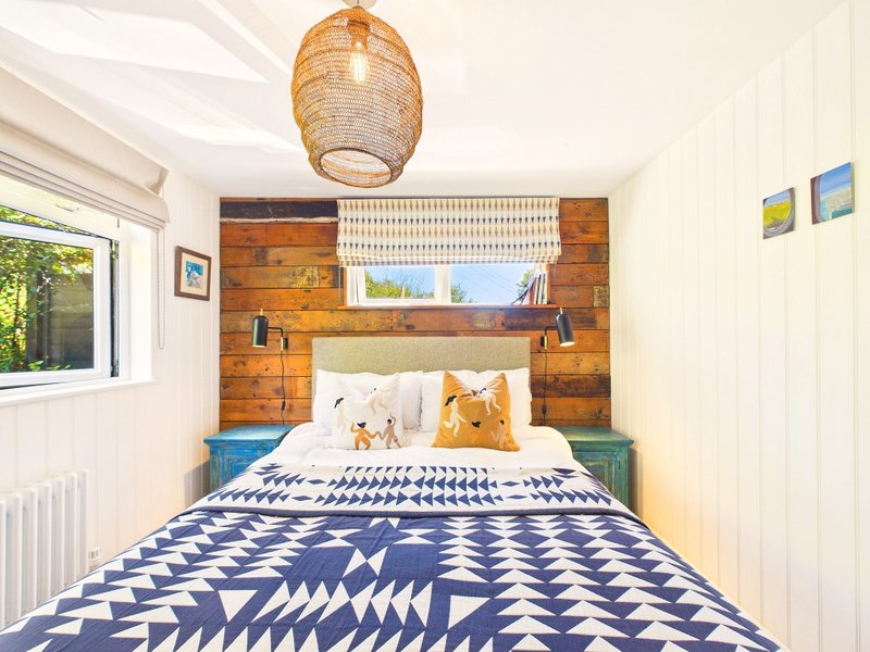 Modern bedroom with double bed, geometric patterned duvet, wooden headboard and woven pendant lamp