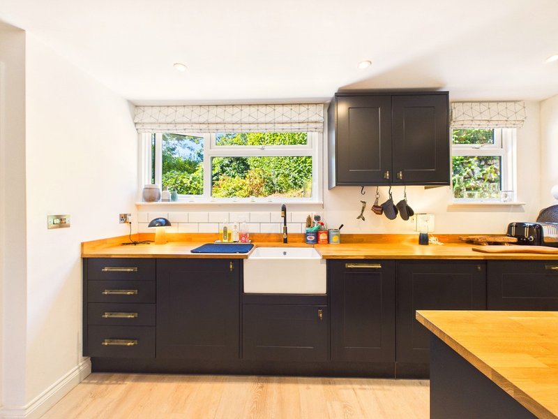 Modern kitchen with black cabinetry, yellow countertops, farmhouse sink and garden view windows