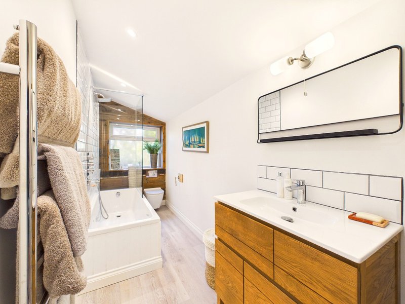 Modern bathroom with wooden vanity, white subway tile, mirror, and towel rail
