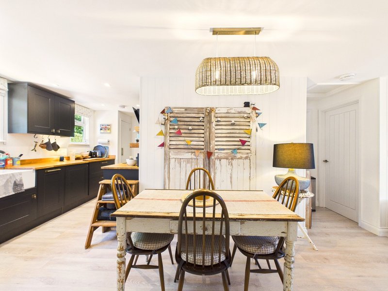 Open-plan kitchen and dining area with wooden table, chairs, pendant lighting and black cabinetry