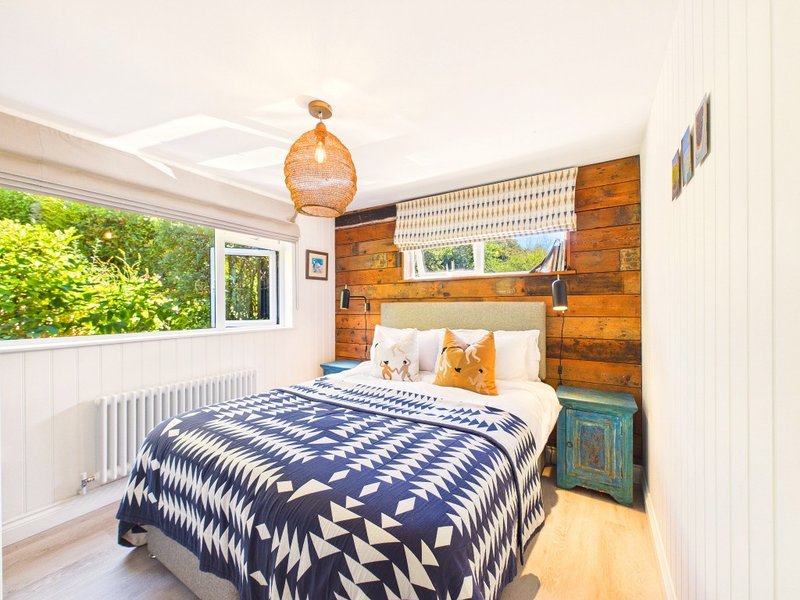 Bedroom with double bed, wooden feature wall, orange pendant light and large window with garden view
