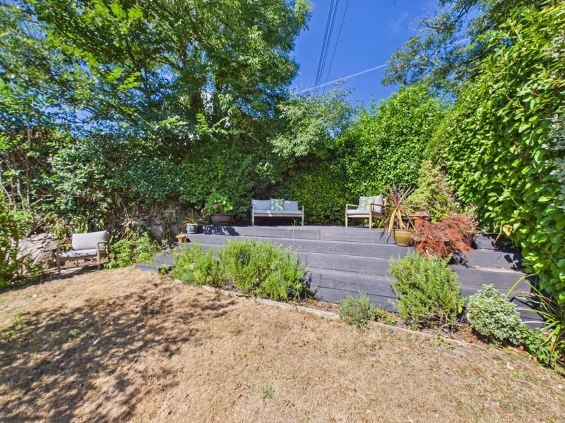 Backyard patio area with decking, seating, lush greenery and mature trees
