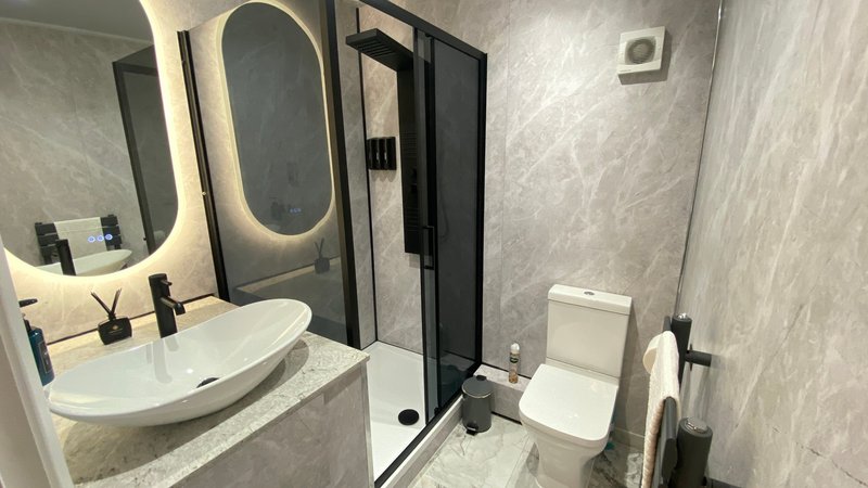Modern bathroom with curved sink, illuminated mirror, shower enclosure and toilet