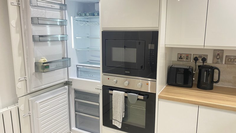 Modern kitchen with white cabinets, integrated appliances, microwave, oven and wooden countertop