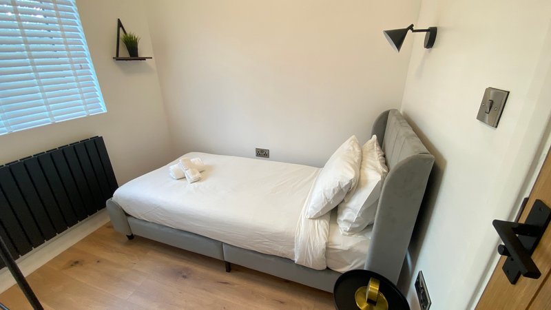Modern bedroom with grey upholstered bed, white bedding, wooden floor and wall-mounted lighting