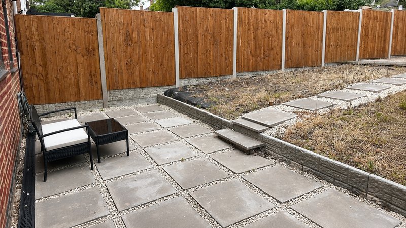 Paved garden patio with wooden fence, garden bed, and outdoor seating