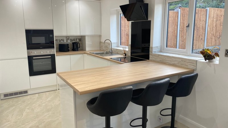 Modern white kitchen with wooden island, black bar stools, stainless steel appliances